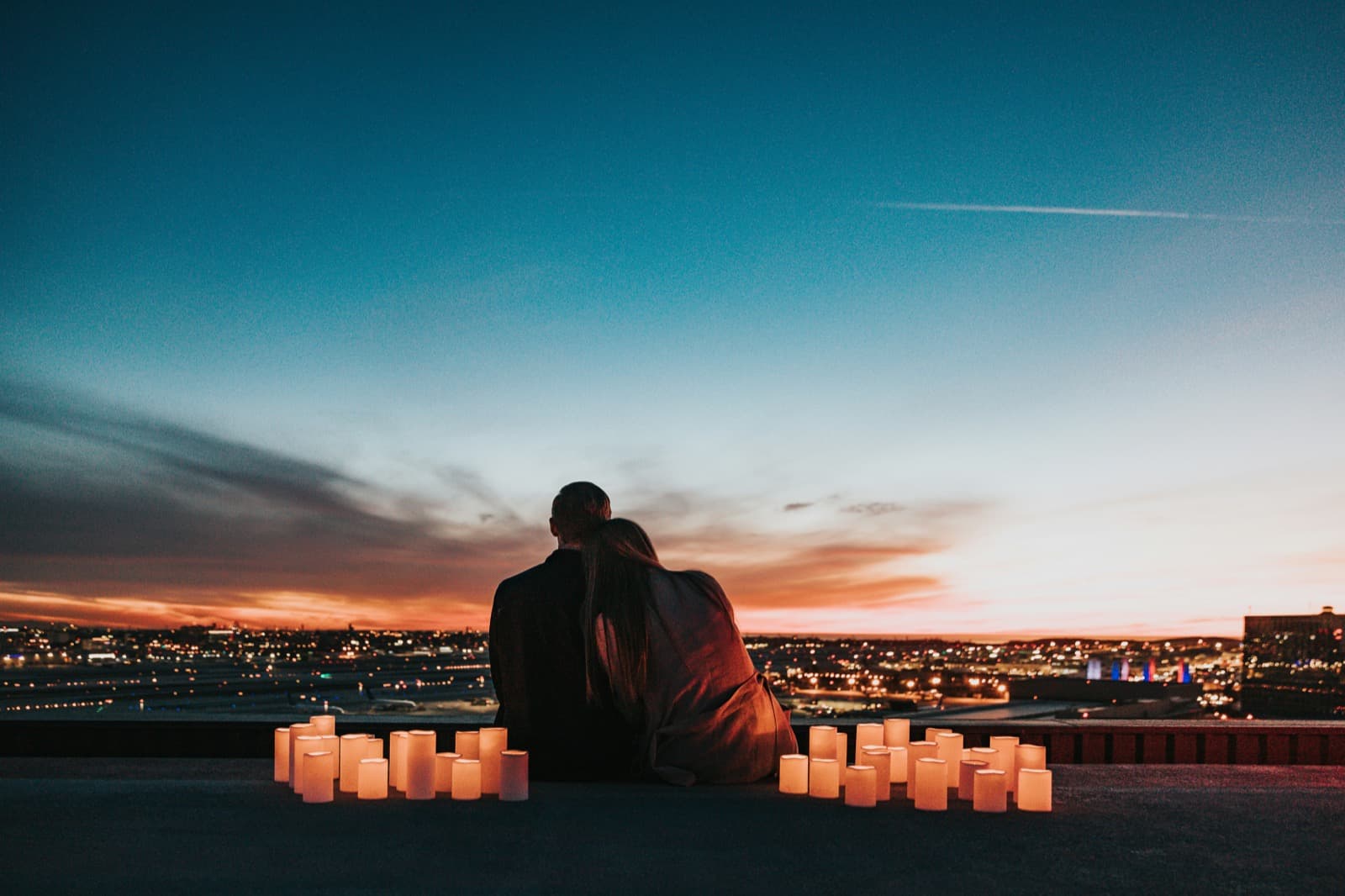 A couple sitting together looking at a city skyline at sunset, representing connection and partnership